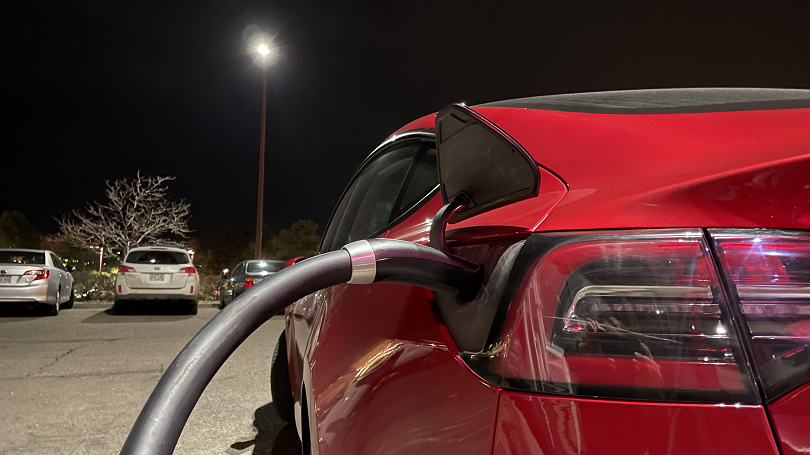 Red electric vehicle connected to a North American Charging Standard (NACS) -- now standardized as SAE J3400 -- direct-current fast charging cable.