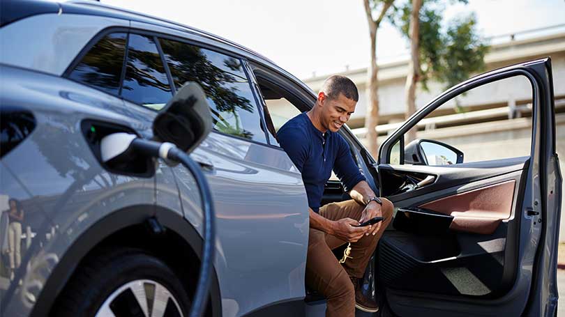 Man looks at his phone while charging an electric vehicle.