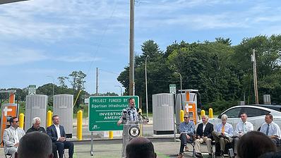 Gabe Klein speaks at podium in open field near charging stations.