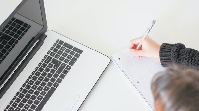 Man writing notes while watching computer